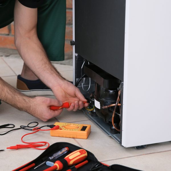 Male technician repairing broken refrigerator indoors, closeup