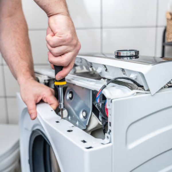 Repairman using a screwdriver disassembles a washing machine for repair